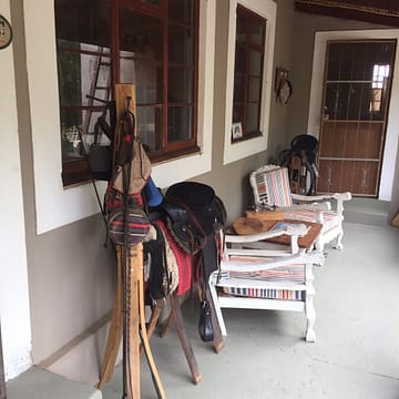 photo0jpg A rustic porch displaying horse saddles and gear alongside striped chairs, characterized by wooden details and warm, inviting colors.